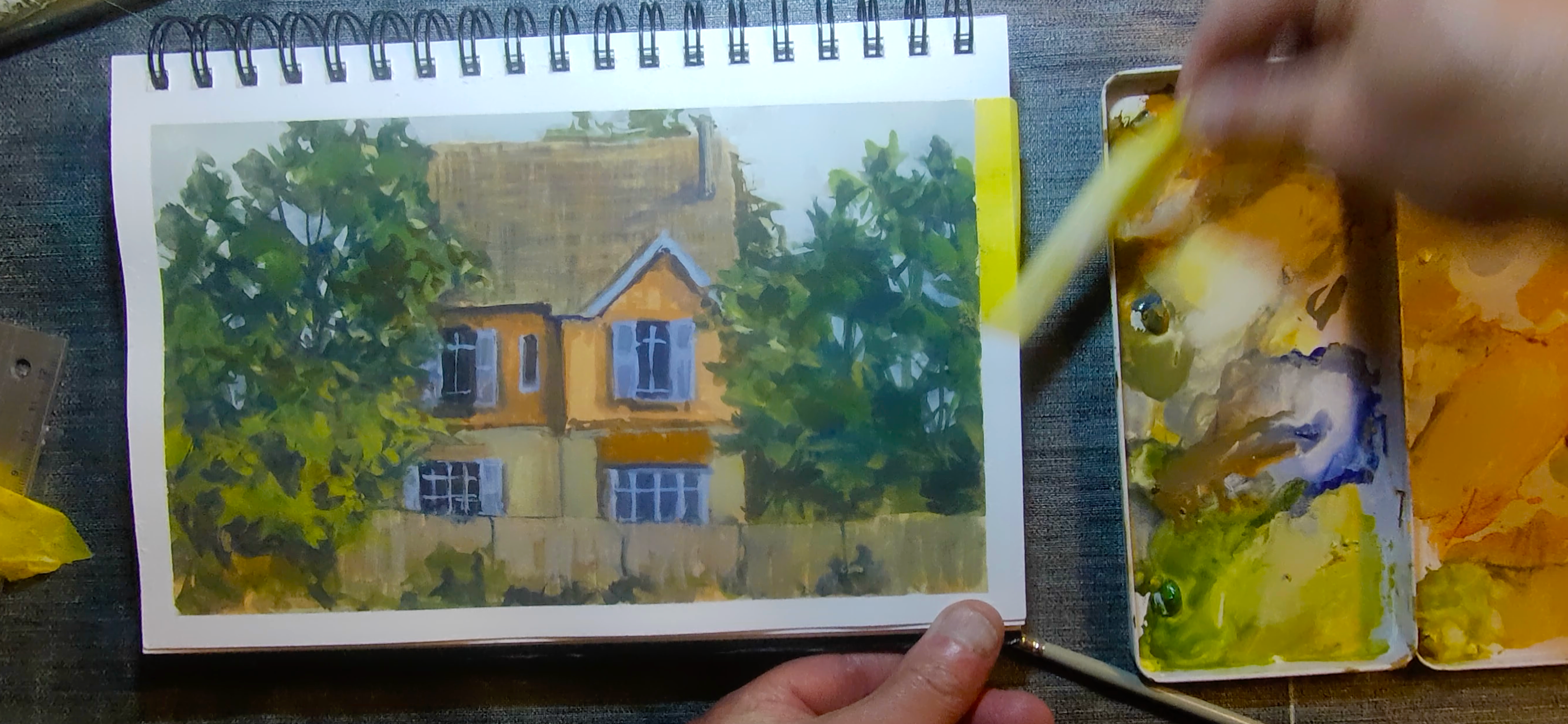 L’adhésif en fin de peinture à la gouache Carnet de gouache représentant une maison, avec l’adhésif encore posé sur le bord droit en fin de travail
